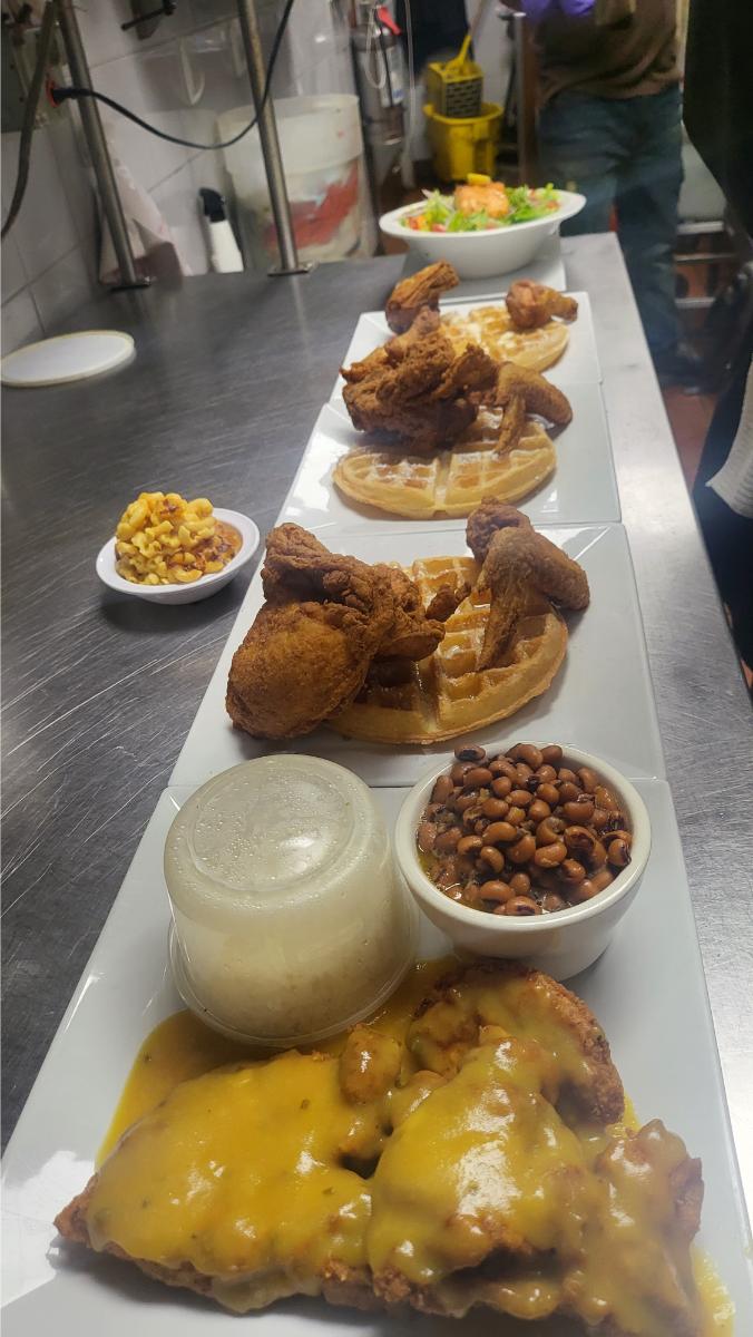 Lineup of soul food plates including chicken and waffles, black-eyed peas, and smothered meat with gravy